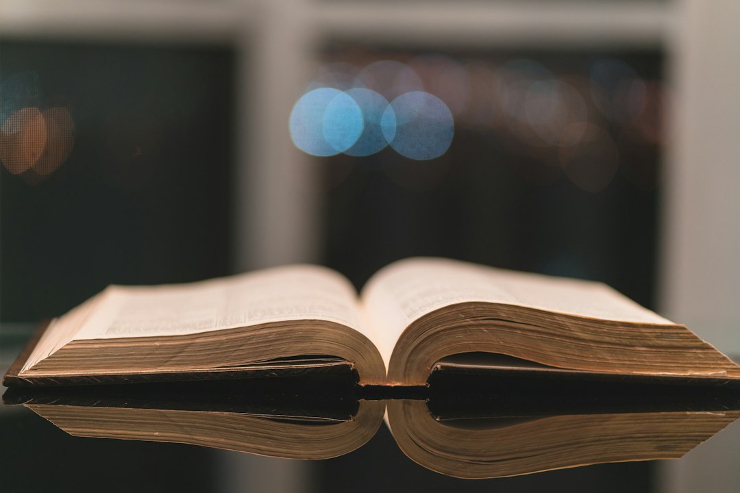 An open book on a reflective surface with blurred lights in the background.